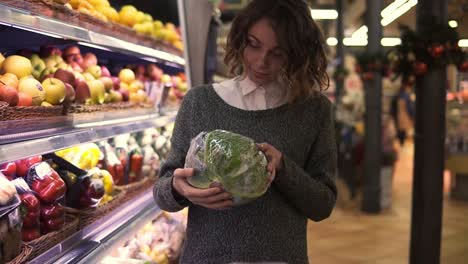 mujer joven en un supermercado moderno eligiendo repollo grande en el departamento de verduras orgánicas y ponerlo en un carrito. mujer sana comprando alimentos verdes. concepto fresco, variedad, chica vegetariana en la tienda de comestibles