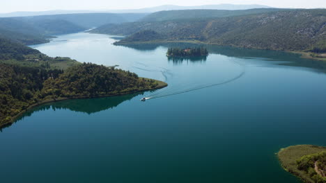 tourist boat sailing in the blue river away from visovac monastery in croatia - aerial shot