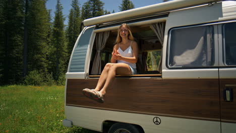 Young woman making peace sign in a camper van window in a forest