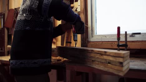 un hombre está usando un taladro para perforar agujeros en una pila de madera asegurada en pinzas en indre fosen, condado de trondelag, noruega - de cerca
