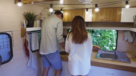 Two-lovers-drink-hot-drinks-from-the-gray-cups-that-they-hold-in-their-hands.-A-beautiful-girl-and-a-young-man-are-standing-in-a-small-kitchen-of-their-trailer-truck-and-enjoying-recreation