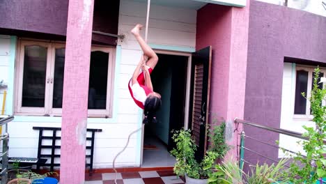 Front-view-of-a-young-Indian-girl-getting-ready-for-yoga-by-climbing-on-a-rope-at-her-home