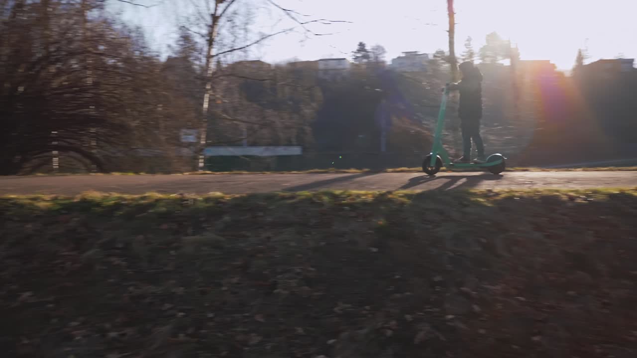 Un bambino sfreccia veloce in monopattino elettrico attraverso un parco cittadino soleggiato.