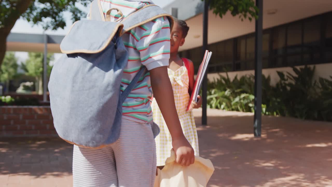 video de un niño y una niña afroamericanos felices con bolsas de escuela dando los cinco fuera de la escuela