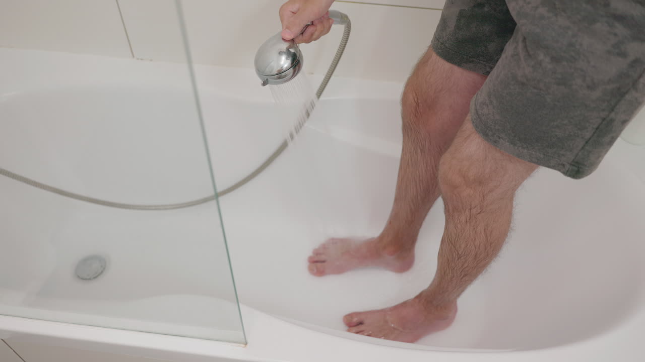Person cleaning a bathtub with a shower head