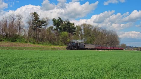 view of a steam passenger train approaching blowing smoke and steam on a beautiful spring day