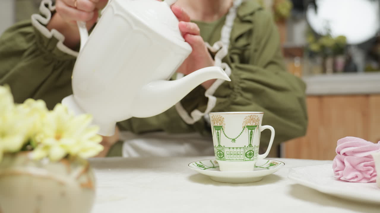 Close up of cake flower as lady pours tea into her glass cup while drinking from it, enjoying relaxing moment with tea, dessert, and peaceful ambiance at cozy kitchen table