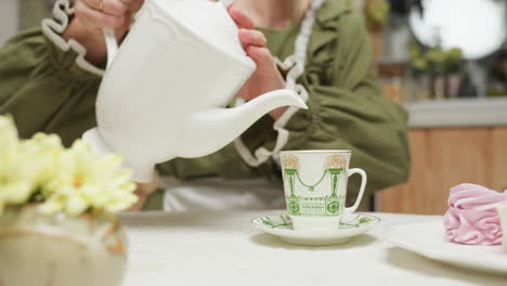 close up of cake flower as lady pours tea into her glass cup while drinking from it, enjoying relaxing moment with tea, dessert, and peaceful ambiance at cozy kitchen table