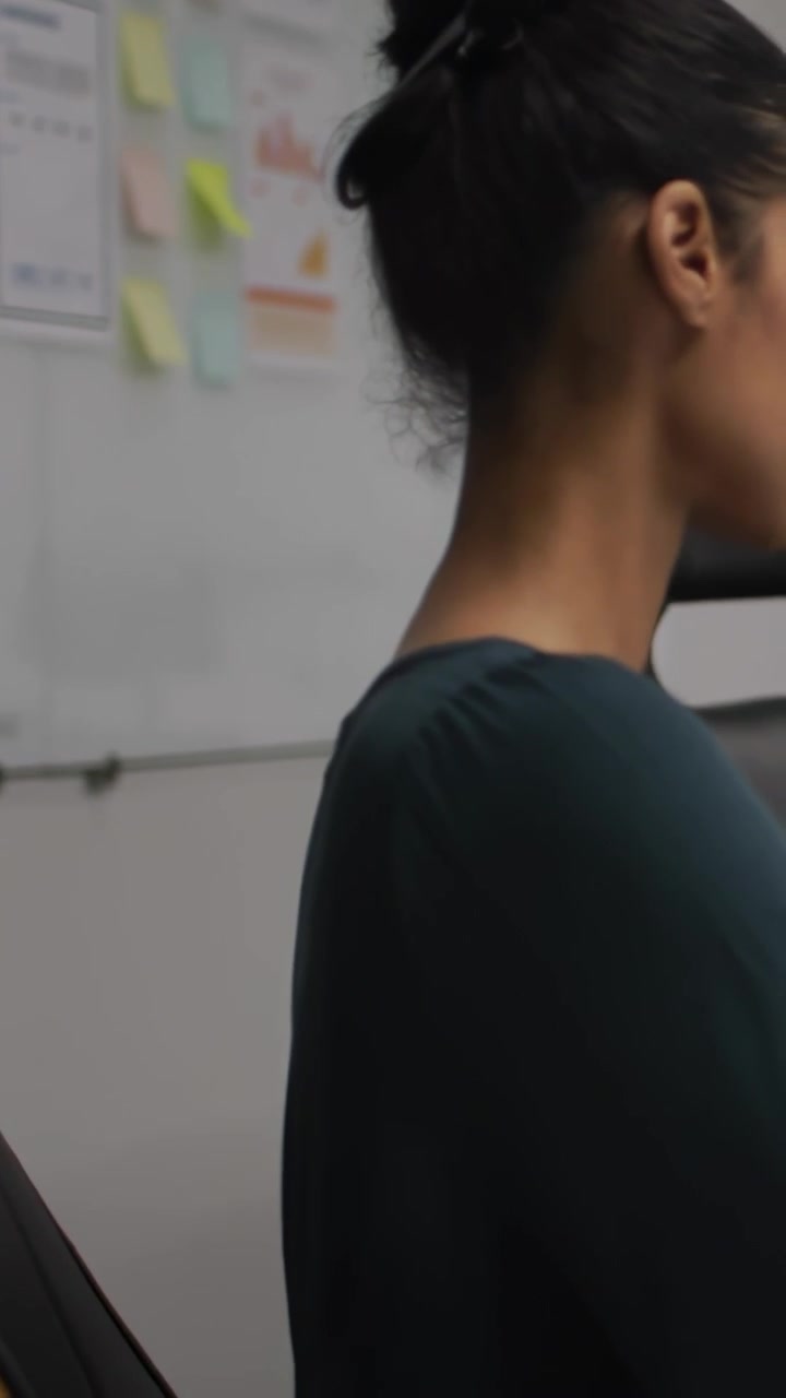 Vertical video: Woman leaning at desk hearing off-frame prompt, animated notes popping on board