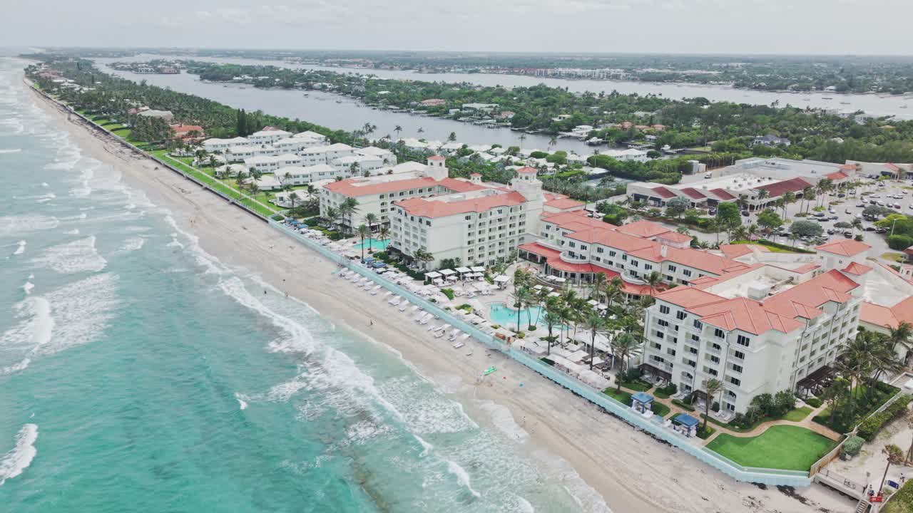 Aerial: beach and turquoise water of Atlantic Ocean with cloudy weather during the day in West Palm Beach, Florida, USA, pan drone shot