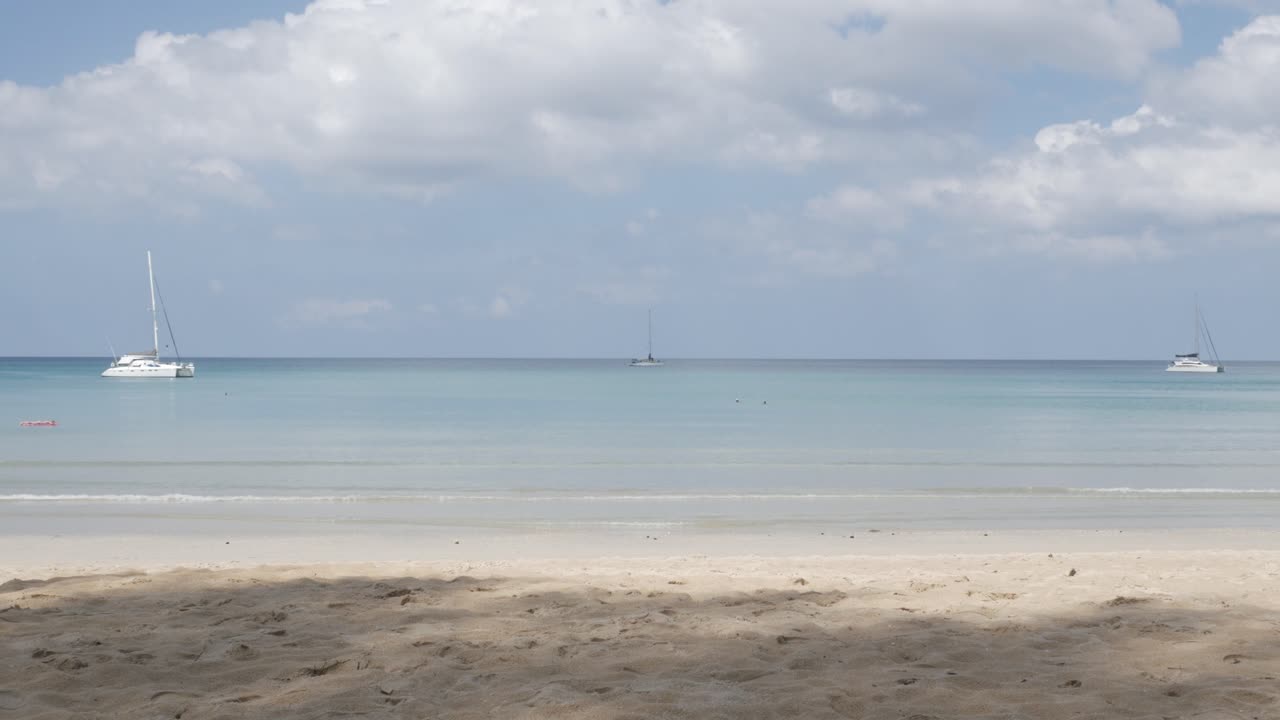 la playa con algunos yates en el mar, arena blanca y olas de un mar tranquilo durante el día soleado