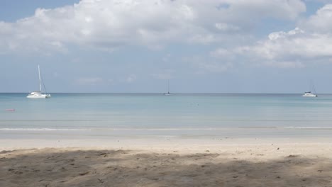 the beach with a few yachts in sea, white sand and wave from peaceful sea in sunshine daytime