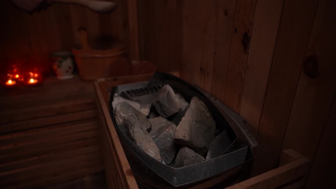 Wooden ladle pouring water onto hot sauna stones inside a wood-paneled sauna room