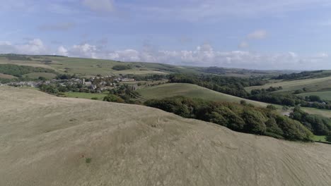 la antena de seguimiento bajo avanza rápidamente por encima de una colina para revelar el pueblo de abbotsbury, en la campiña de dorset