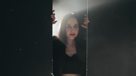 serene woman in black outfit framed by a doorway, bathed in soft light with a slow camera zoom as she smiles gently