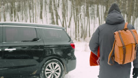 man putting wool blankets and backpack in car boot before leaving for a winter road trip