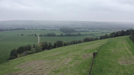 AERIAL---People-walking-in-South-Downs-Way,-East-Sussex,-United-Kingdom,-rising-shot