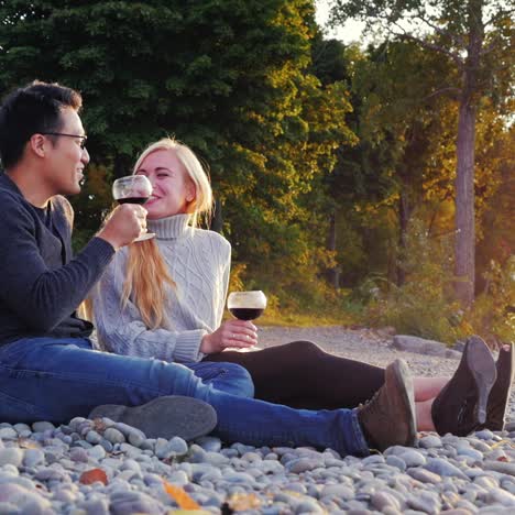 a young couple rests on a pebble beach drinking wine