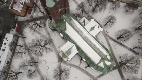 Rotating-birds-eye-view-of-vibrant-green-and-red-Saint-Clare-church-in-winter-landscape