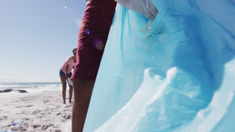 una pareja afroamericana con bolsas de basura y recolectando basura de la playa