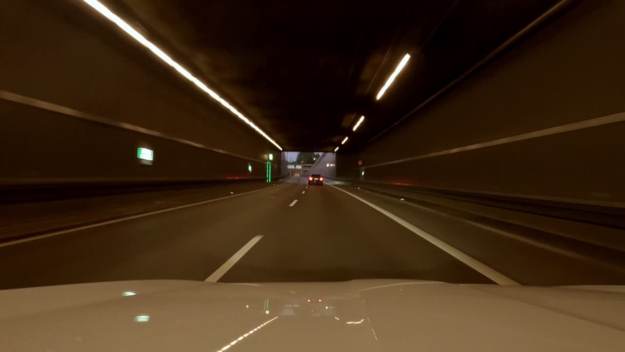 Drive through Munich, a bavarian capital trip by car at the evening. Speeded up from the engine hood view at the late evening with illuminated lanterns and modern buildings.