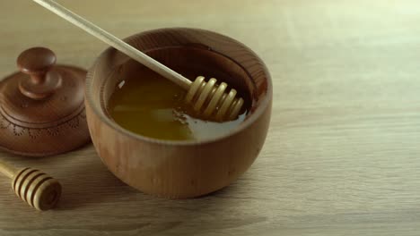 Honey-dripping,-pouring-from-honey-dipper-in-wooden-bowl.-Close-up.-Healthy-organic-Thick-honey-dipping-from-the-wooden-honey-spoon,-closeup.-4K-UHD-video-footage.-Slow-motion