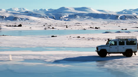 white jeep cruising down icy and snowy road, daytime iceland side profile aerial view