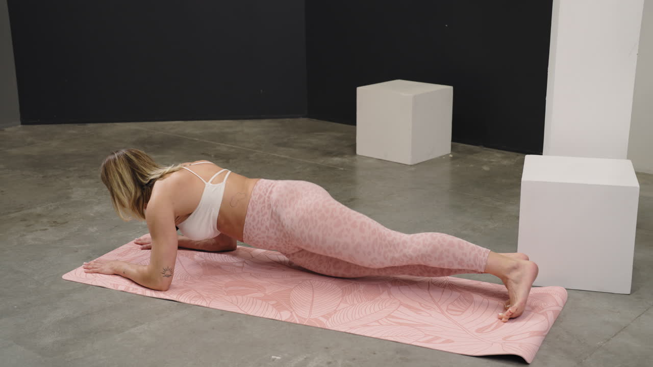 Athletic woman holding a plank position on a pink yoga mat for core muscle training, rearview of hips swinging to each side in leggings