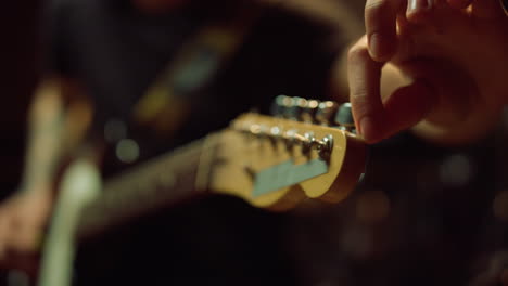 Guitarrista-Girando-Perillas-En-El-Diapasón-En-El-Estudio.-Hombre-Sujetando-La-Guitarra-En-El-Pasillo.