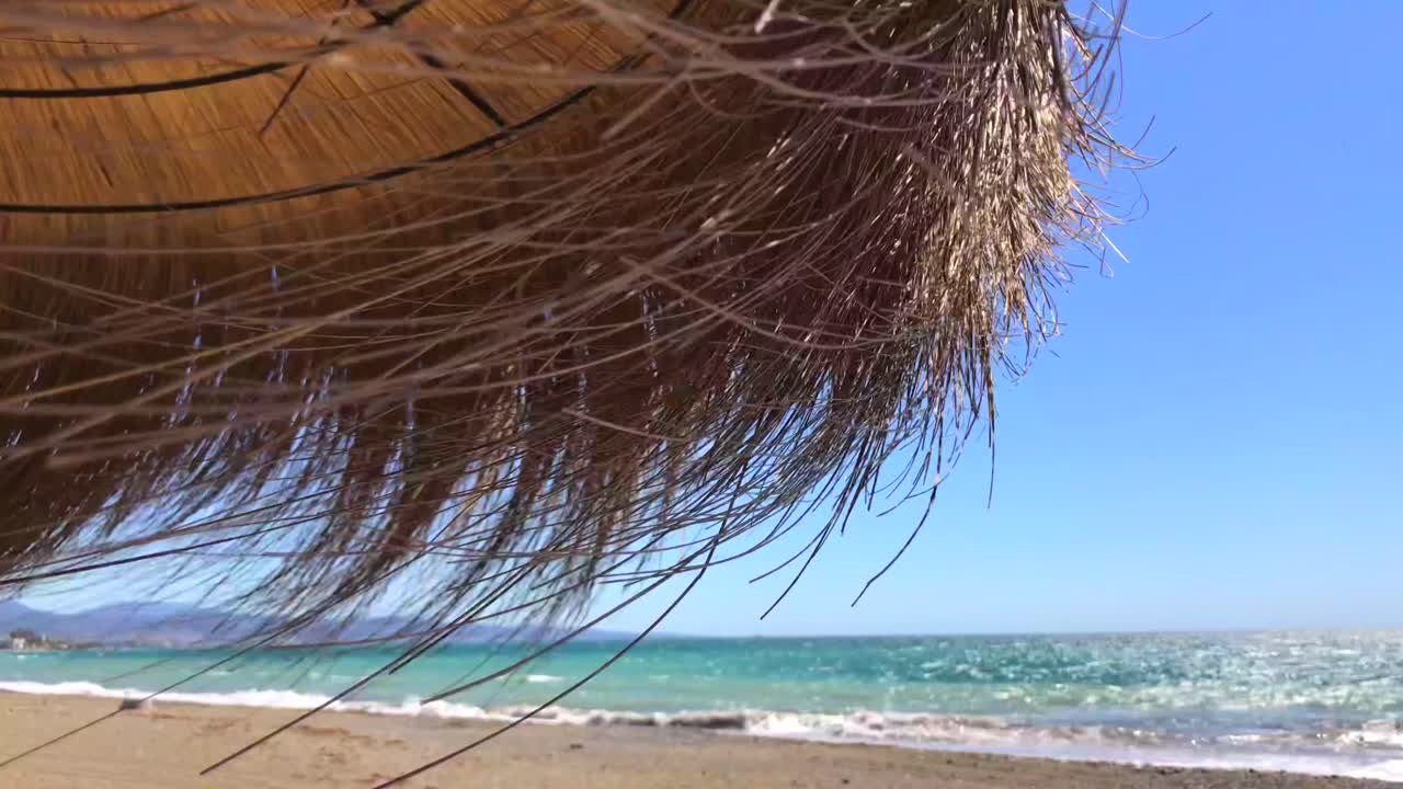 sombrilla tiki con techo de paja en una playa ventosa con vista al mar en un lugar tropical, marbella malaga españa