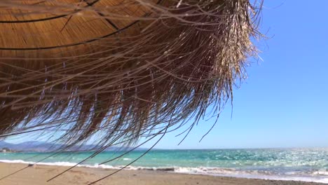 sombrilla tiki con techo de paja en una playa ventosa con vista al mar en un lugar tropical, marbella malaga españa