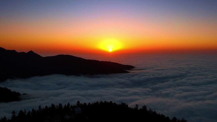 Tramonto mozzafiato su un vasto paesaggio coperto da una fitta coltre di nuvole. Scure sagome di montagne spuntano dalle nuvole