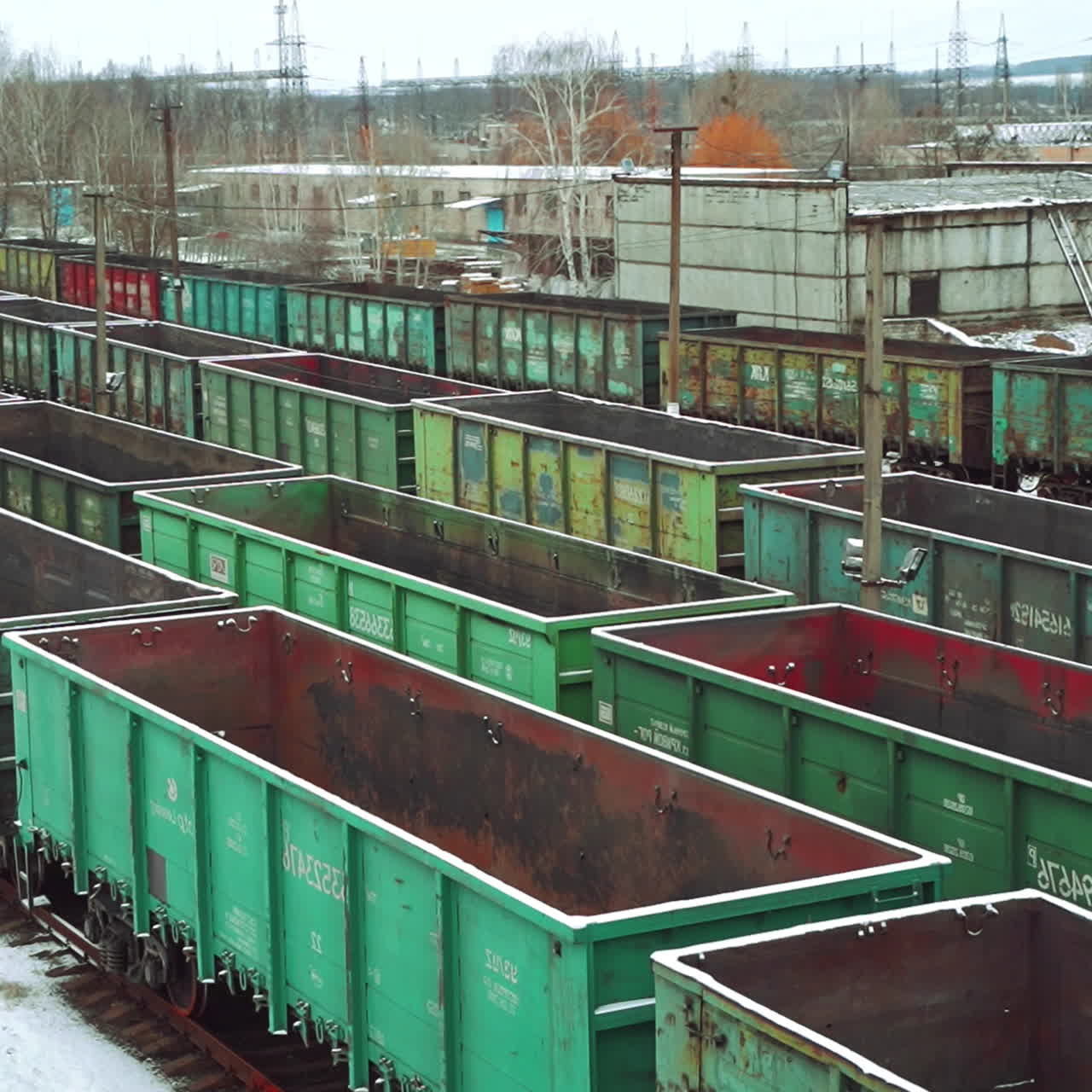 Aerial view on a huge number of iron containers of different colors located at the final station on the background of a freight train, which is moving in their direction. Close-up.