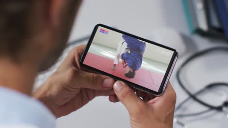 composición de un médico masculino viendo un partido de judo en un teléfono inteligente