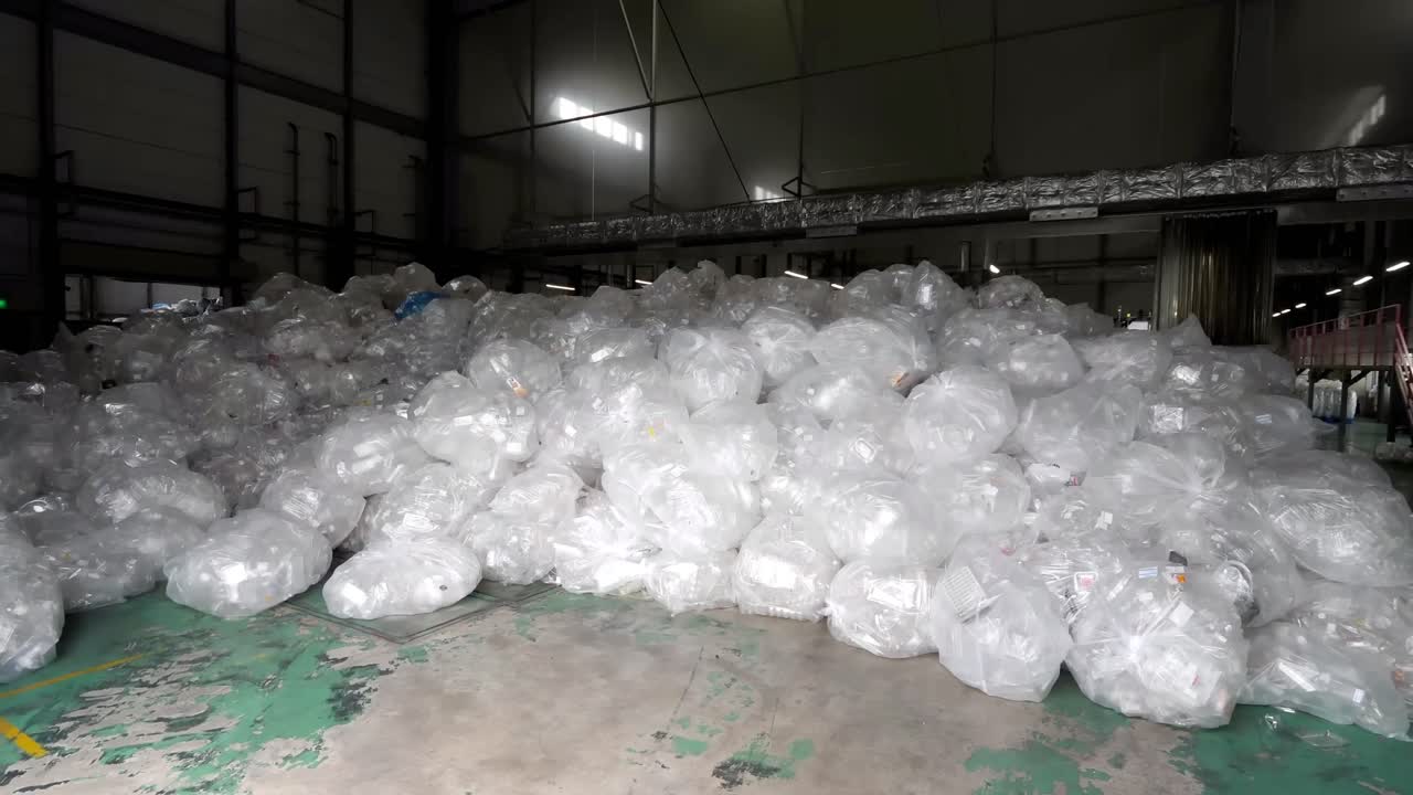 A large quantity of used plastic boxes, wrapped in plastic bags, is stored in a spacious warehouse.