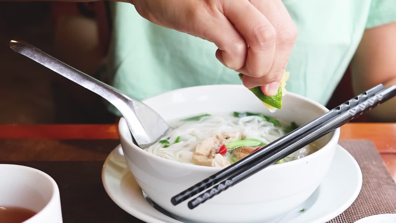 A person squeezes lime into a bowl of noodle soup, enhancing its flavor with citrus.
