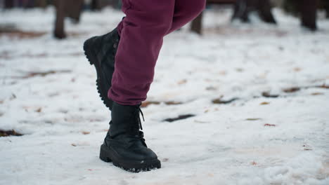 vista lateral de una persona con botas negras saltando de derecha a izquierda en un terreno cubierto de nieve, el entorno de invierno destaca el movimiento, el calzado robusto y la atmósfera estacional nítida