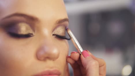 artista de maquillaje aplicando maquillaje de sombra de ojos dorada a los ojos del modelo. vista de cerca