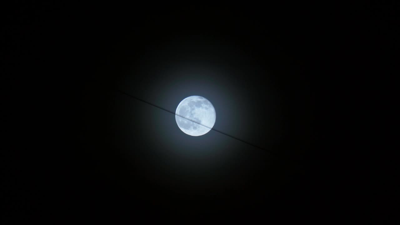 la luna llena es azul contra el fondo del cielo negro de la noche, un alambre colgado de los edificios