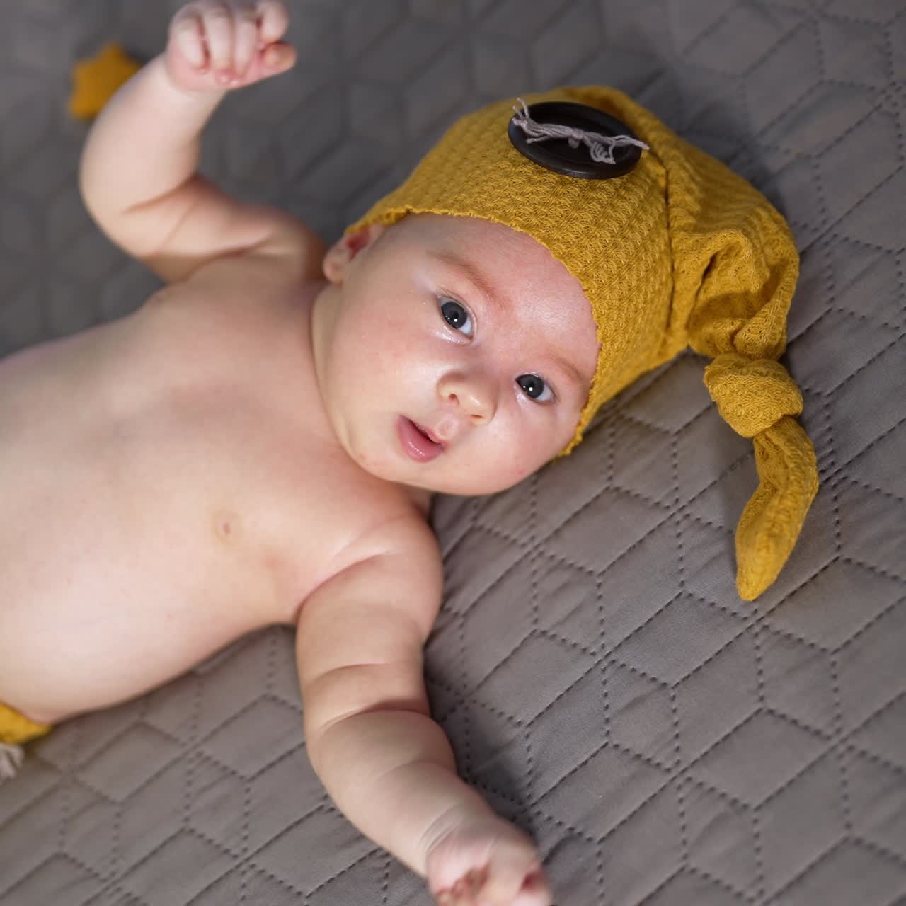 Cute child in a yellow cap and pants. Baby with naked tummy lying on the bed. Little toy stars around the child