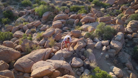 Man-climbing-up-rocks-in-the-desert,-Joshua-Tree-national-park,-California,-slow-motion-aerial