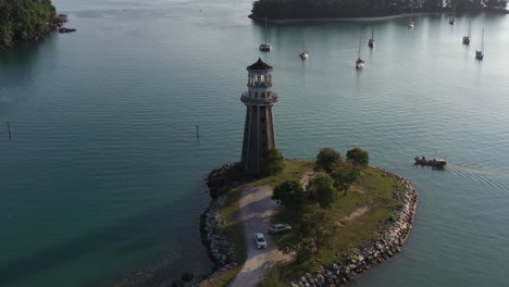 Slow-pan-shot-around-beautiful-promontory-with-perdana-quay-light-house-in-the-center,-local-fishing-boat-cruising-towards-telaga-harbor-marina-at-langkawi-island,-kedah,-archipelago-of-malaysia