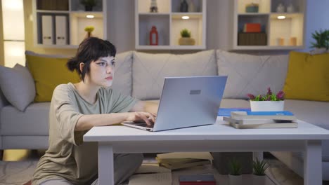 young woman focusing on computer has serious expression. at home at night.