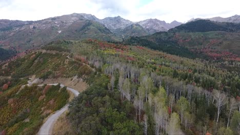 a drone flies across a high mountain ridge road as the snow dusts the mountain tops and trees change into fall colors in utah.
