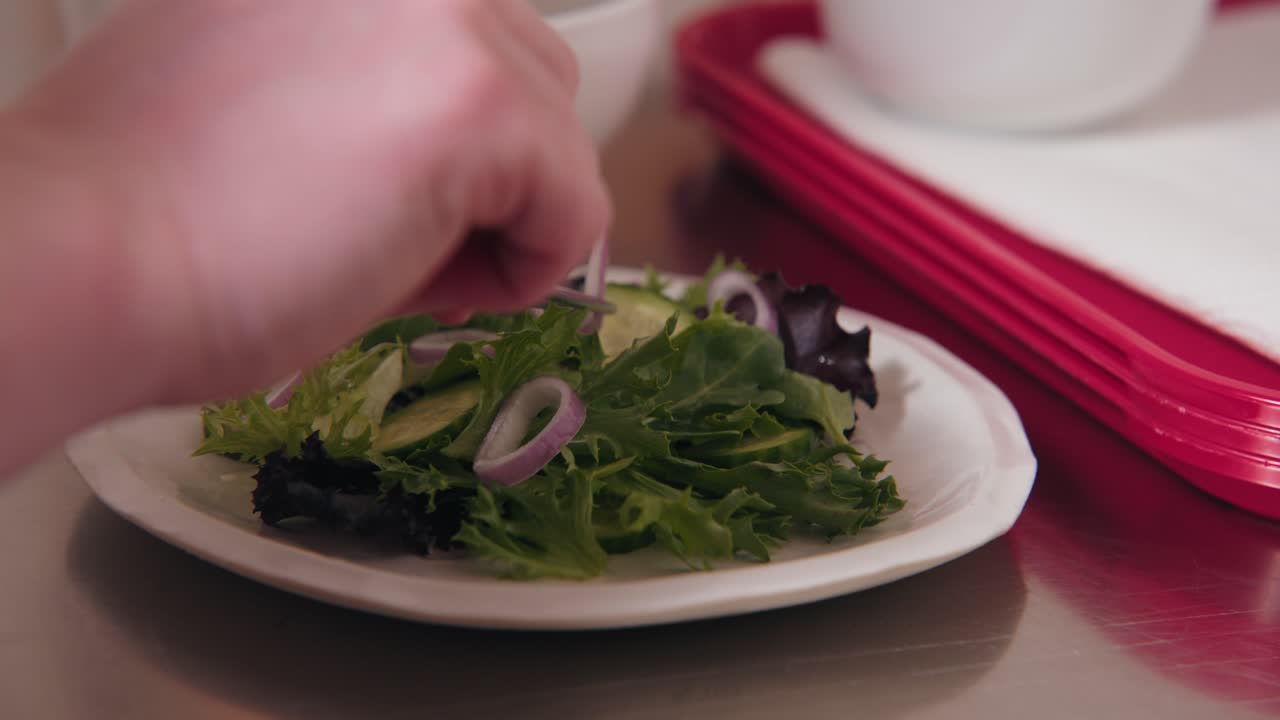 un chef profesional, fotógrafo culinario, artista culinario coloca una fina rebanada de chaloto en un plato de ensalada verde con hojas para una foto de comida con un delicado conjunto de pinzas en un espacio de trabajo de cocina