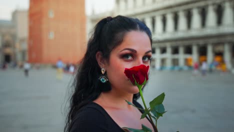 chica con una rosa roja, primer plano, panorámica alrededor de la chica, cabello negro, vestido negro, en la ciudad, edificios en el fondo