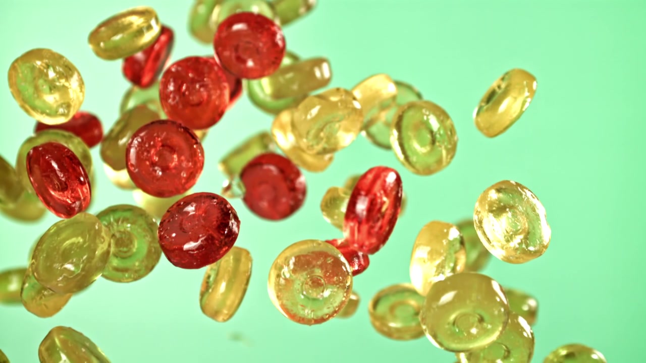 Caramelle rosse e gialle che cadono al rallentatore su sfondo verde