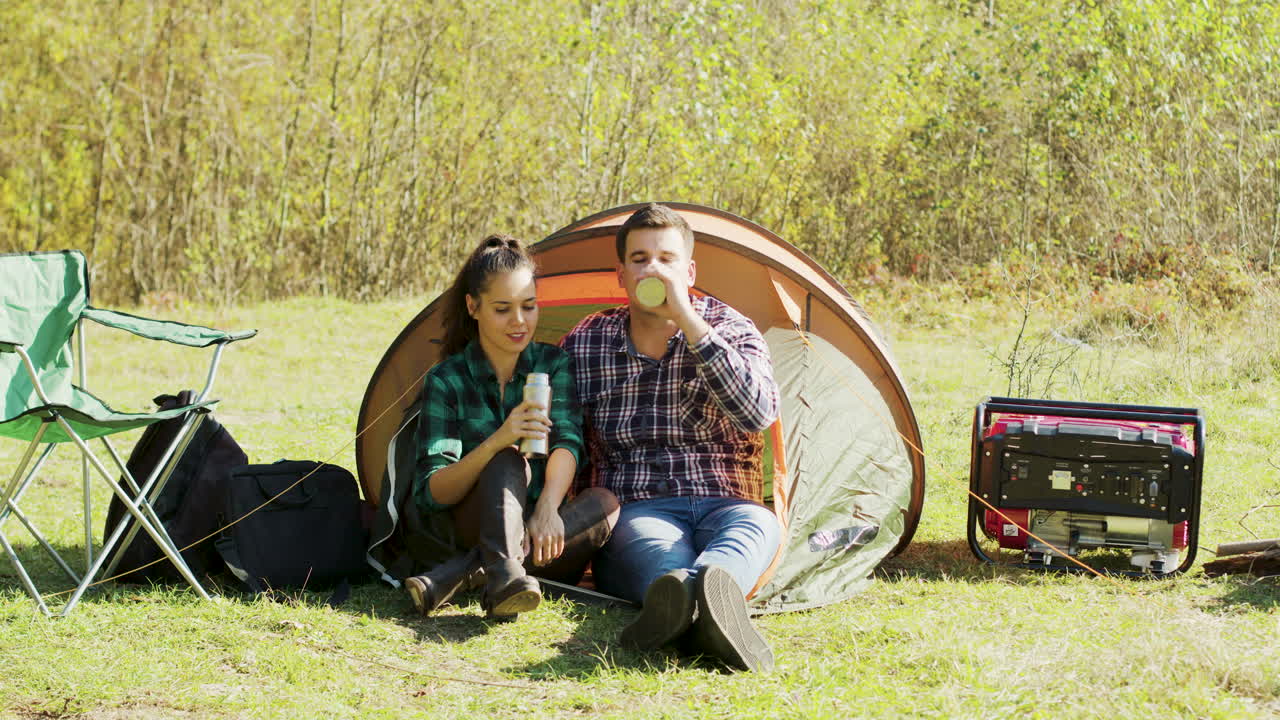 Boyfriend kissing his girlfriend cheek sitting in front of their camping tent