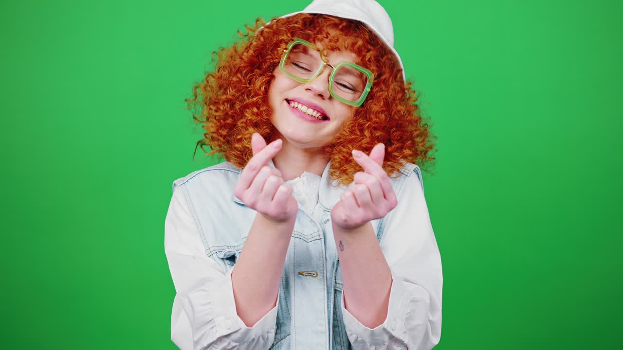 mujer rubia y rizada con gafas y sombrero de panama mostrando corazones con los dedos y sonriendo a la cámara
