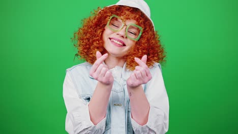 cute redhead curly woman wearing eyeglasses and panama hat showing hearts with fingers and smiling to camera